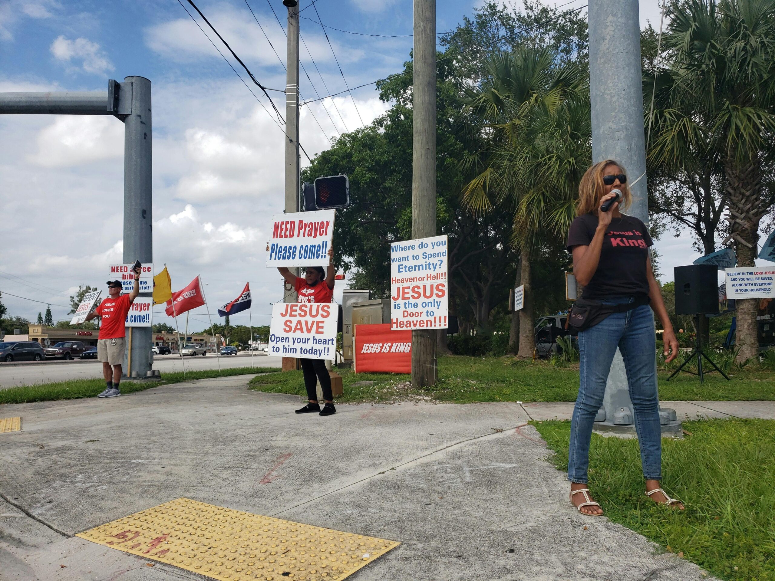 A group of people holding religious signs and preaching on a street corner, inviting passersby to seek prayer and salvation.